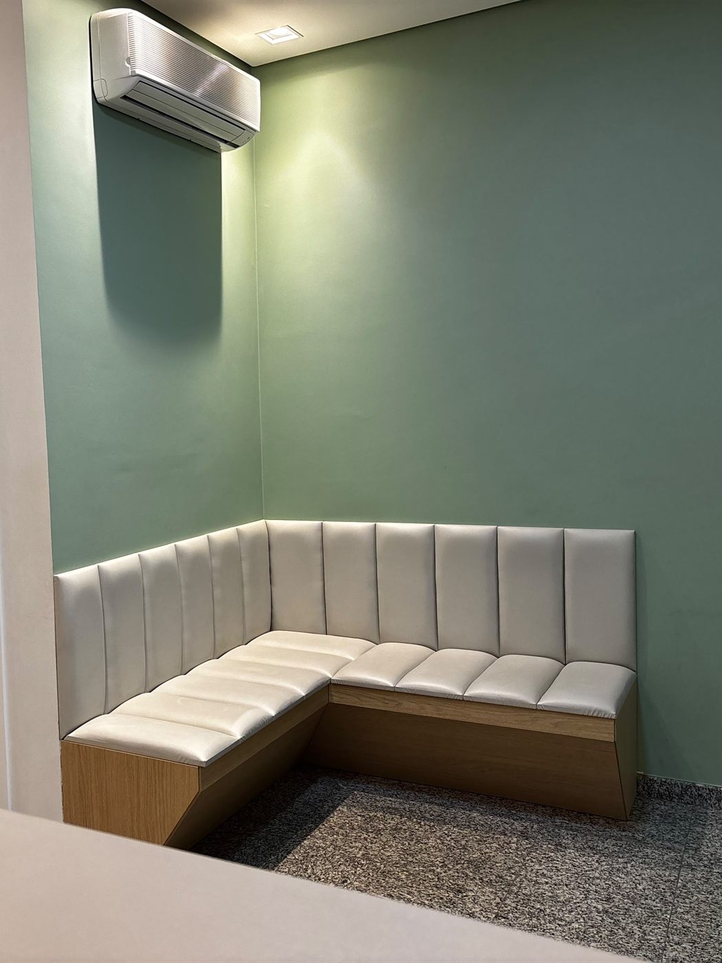 Sala de espera do consultório, com banco estofado em L e parede verde