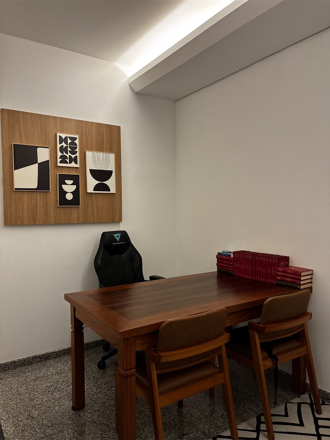 Sala de atendimento do consultório em Joinville, com mesa de madeira e quadros geométricos